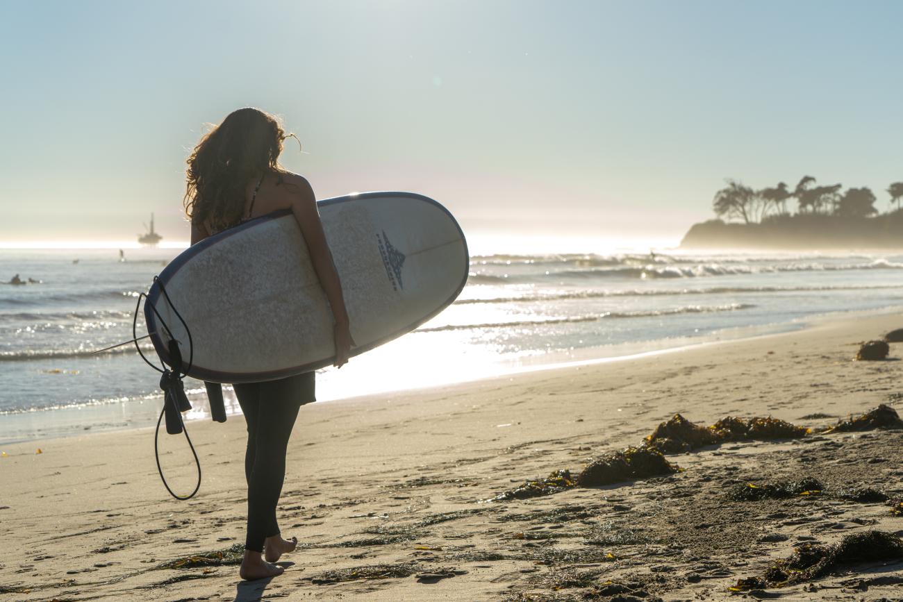 Woman holding surfboard walking on beach