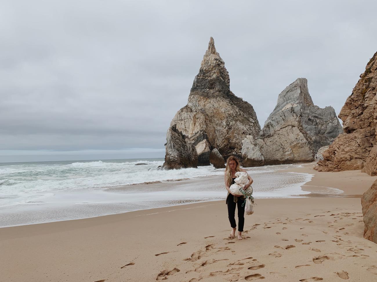 Person walking on beach carrying bags of plastic waste