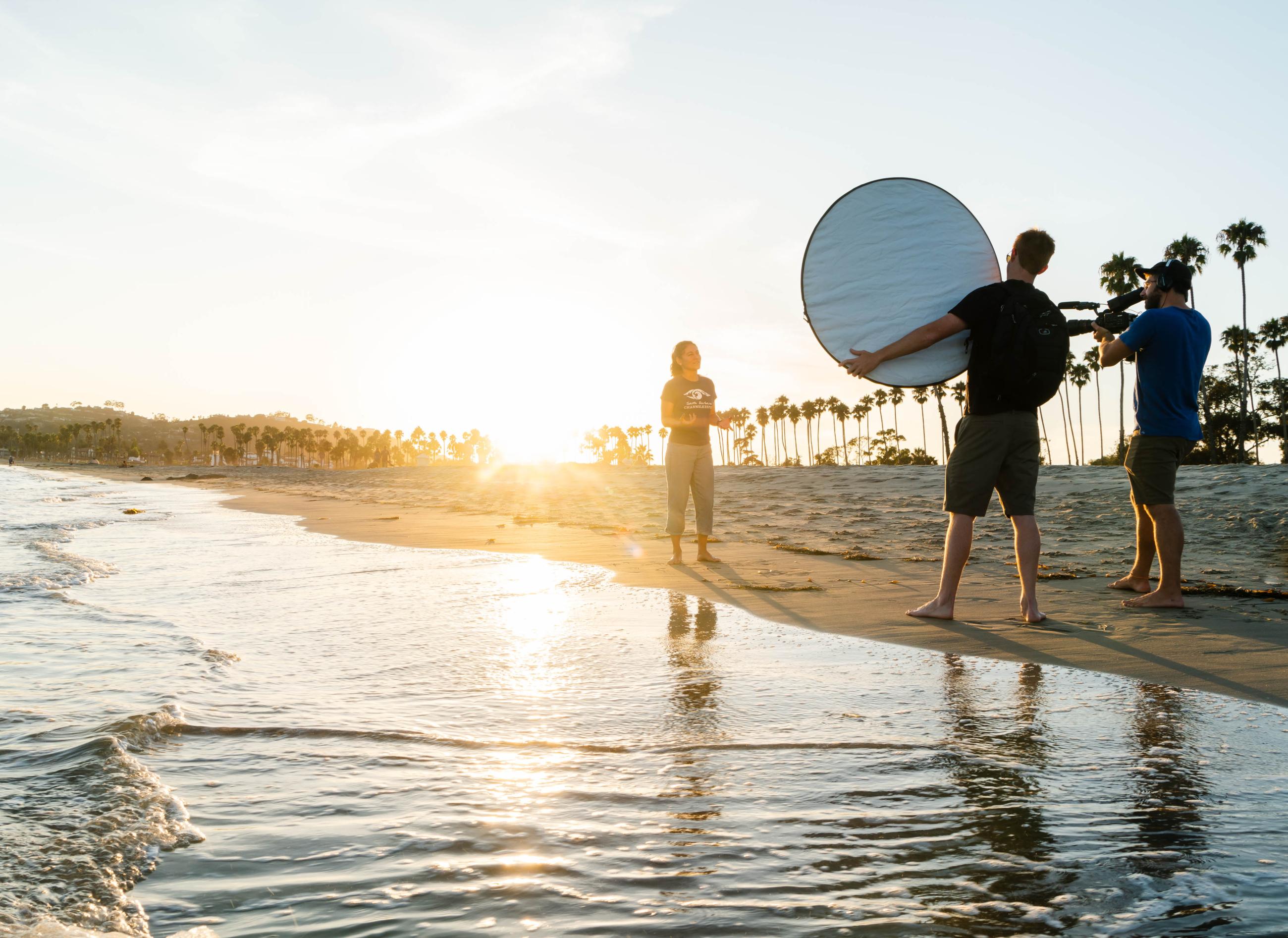 Video crew filming a woman talking on beach