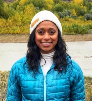 Woman in jacket and beanie standing in front of river