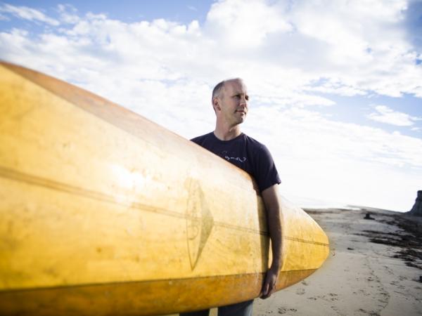 Man (Halpern) holding surfboard on the beach