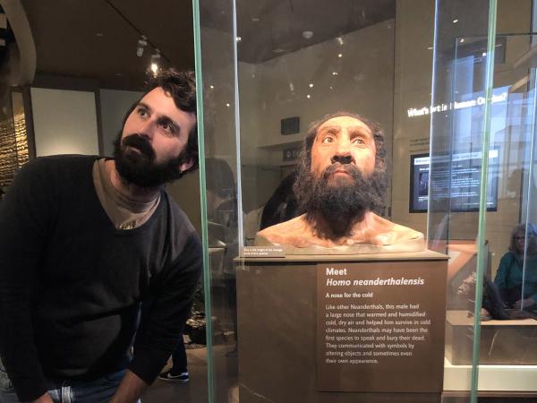 Man places head next to model of "neanderthal man" at museum