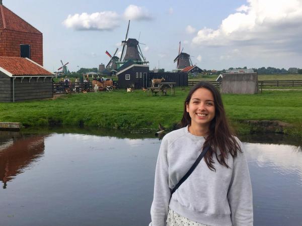 Woman stands in front of landscape with windmills and water