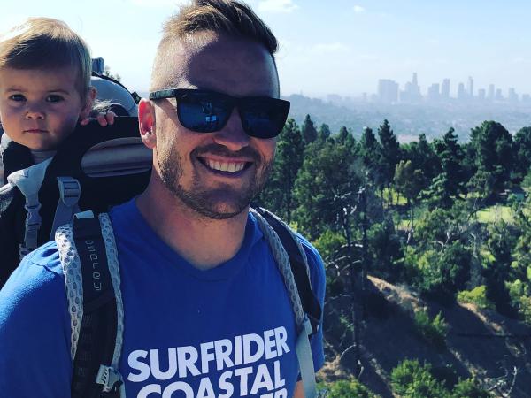 Hiking man with baby in backpack, city in distance