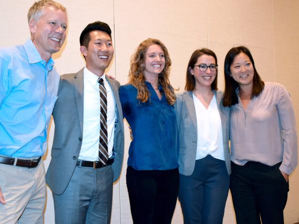 Five people link arms and smile on stage