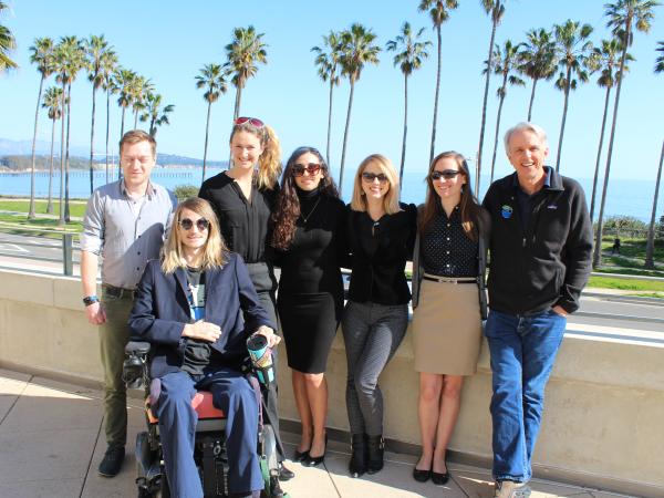 A student group poses with faculty and PhD advisors with an ocean backdrop