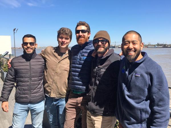 Five men in warm outdoor coats standing by sea shore