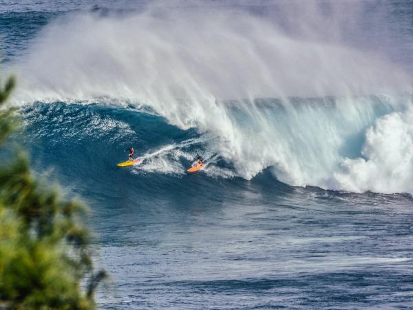 waves crashing on the coastline with two surfers on the wave.