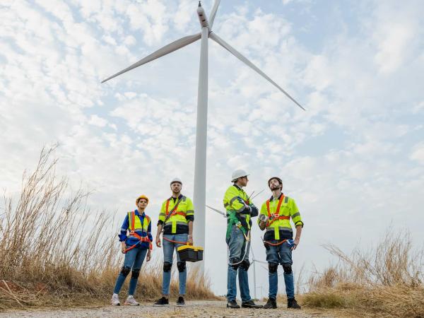 Teamwork engineer wearing safety uniform standing crossed arms at wind turbine